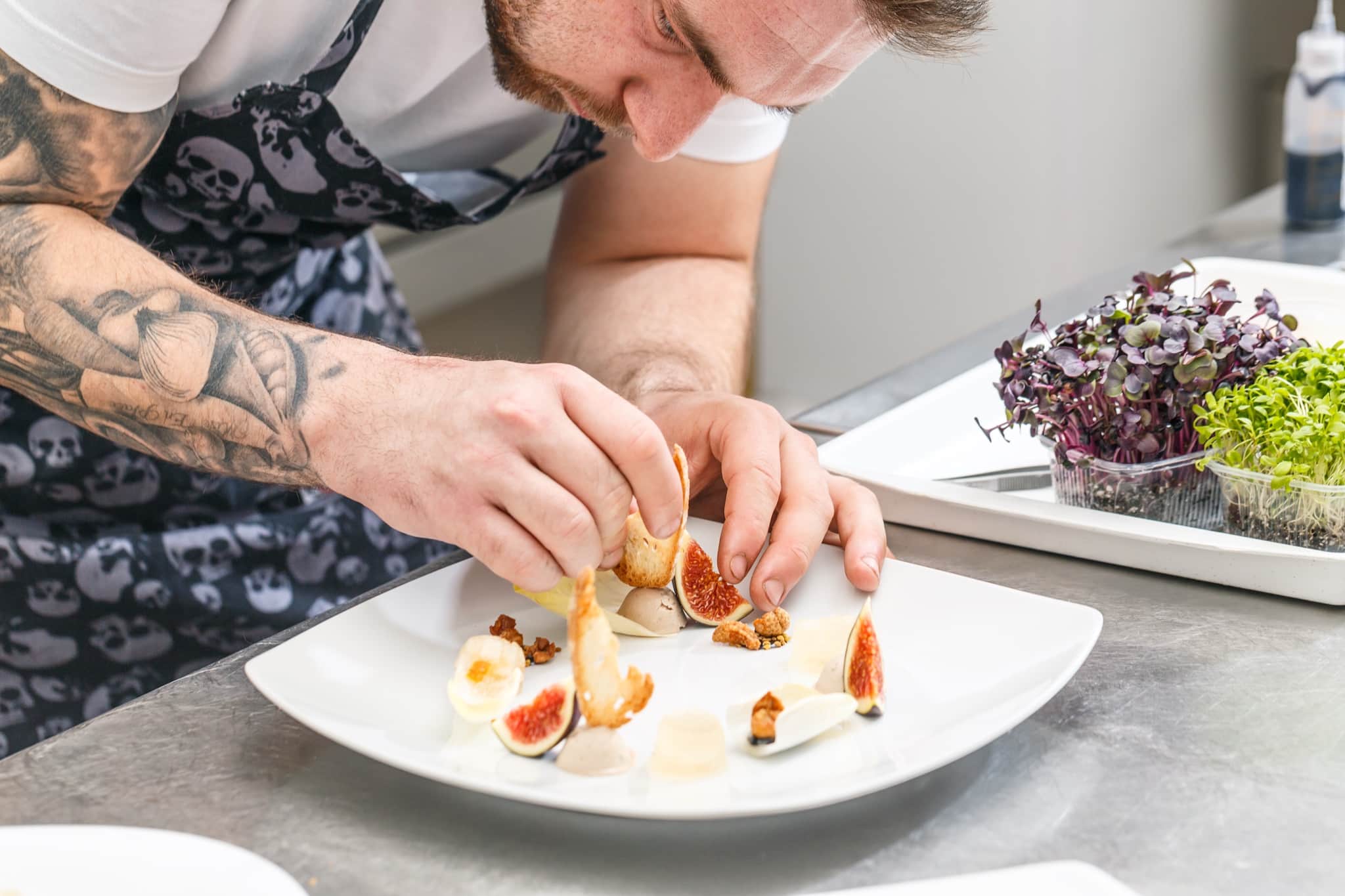 Chef plating an elegant fig and microgreens appetiser on a white plate in a villa kitchen — private chef dinner on Rhodes