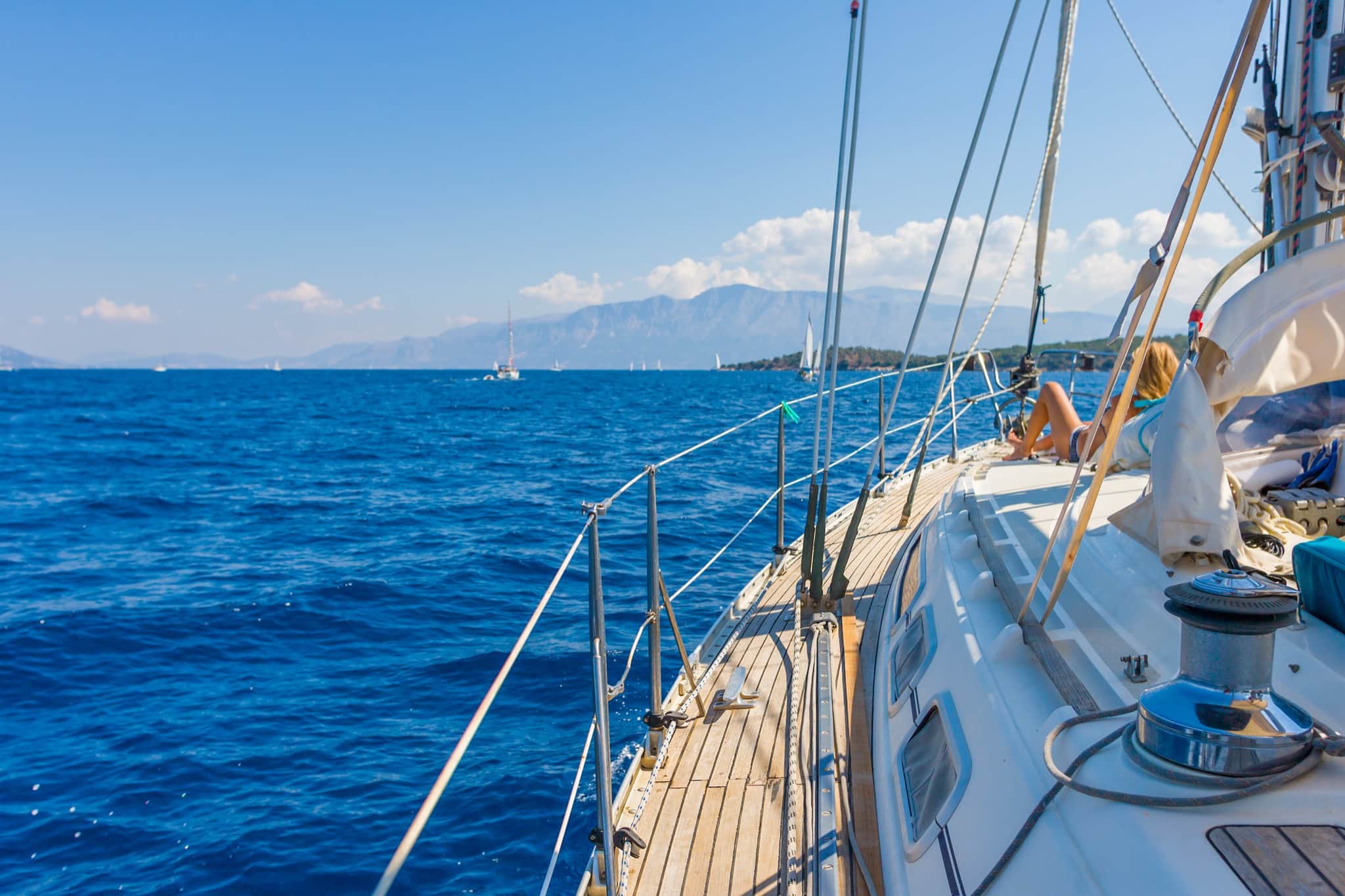View along the teak deck of a sailing yacht under way on deep blue Greek seas with mountains on the horizon — private yacht cruise from Rhodes